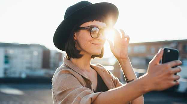 Woman with hat and glasses takes selfie in light