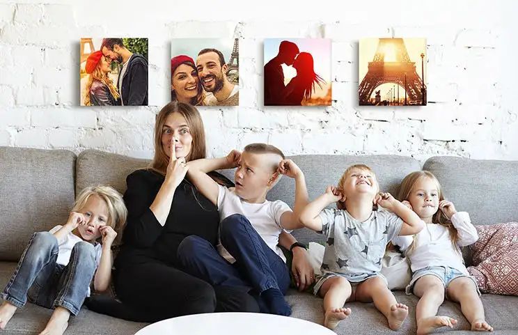 Mom and four young kids sitting on sofa in front of four photo canvases